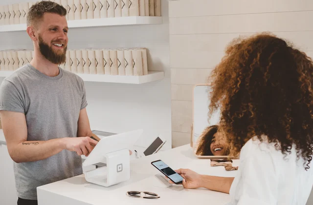 Retail operator helping a customer complete a mobile payment at a checkout counter
